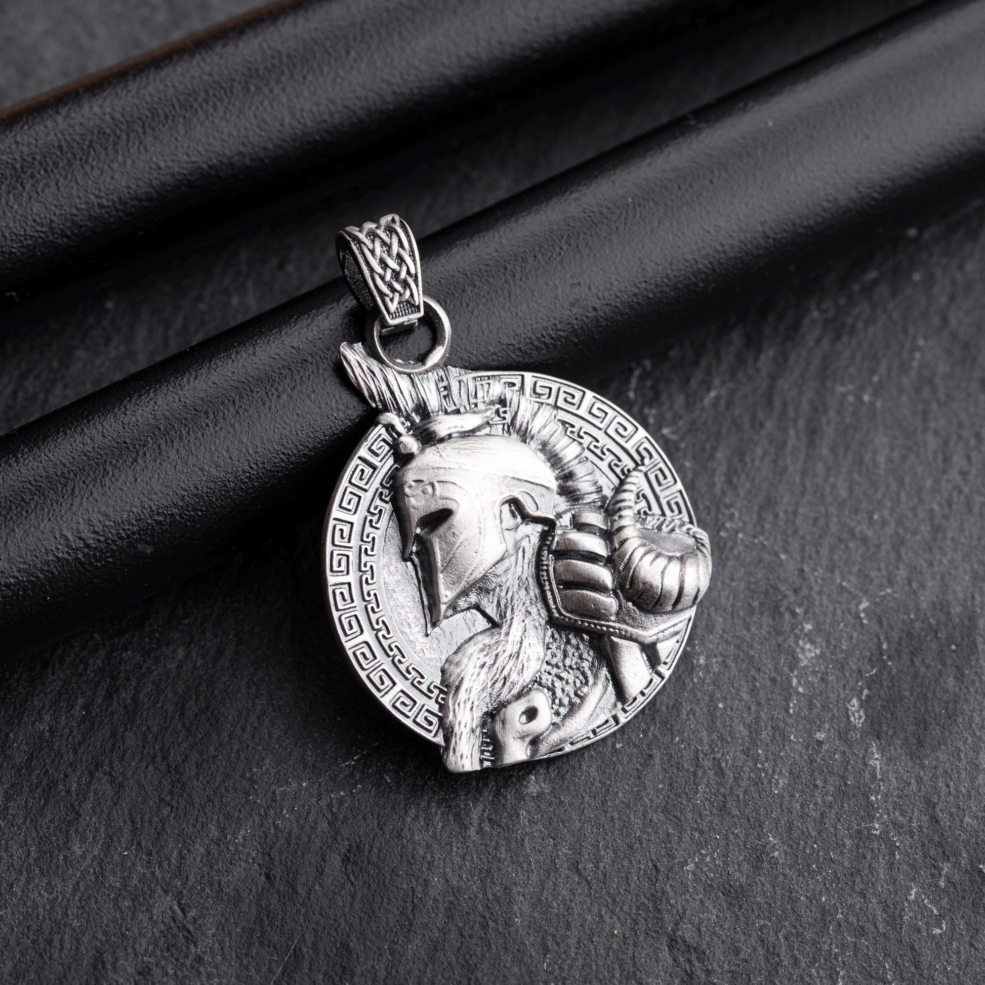 Gladiator Pendant in silver featuring a detailed helmeted warrior profile with a ram's head and intricate braided bail, set against a patterned circular background.