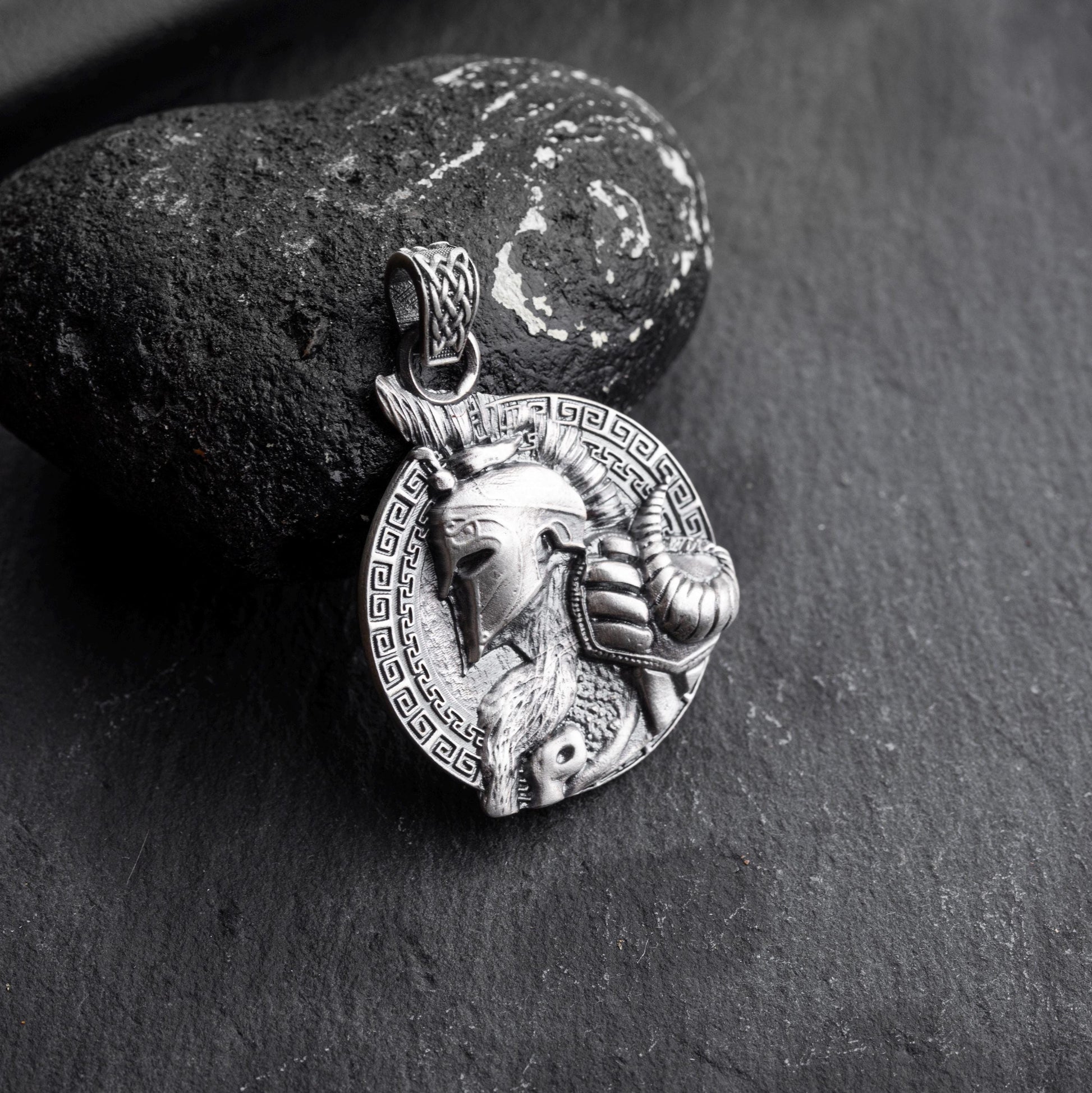 Silver Gladiator Pendant featuring a detailed helmeted warrior design with an ornate circular border, resting against a textured black stone background.