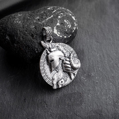 Silver Gladiator Pendant featuring a detailed helmeted warrior design with an ornate circular border, resting against a textured black stone background.