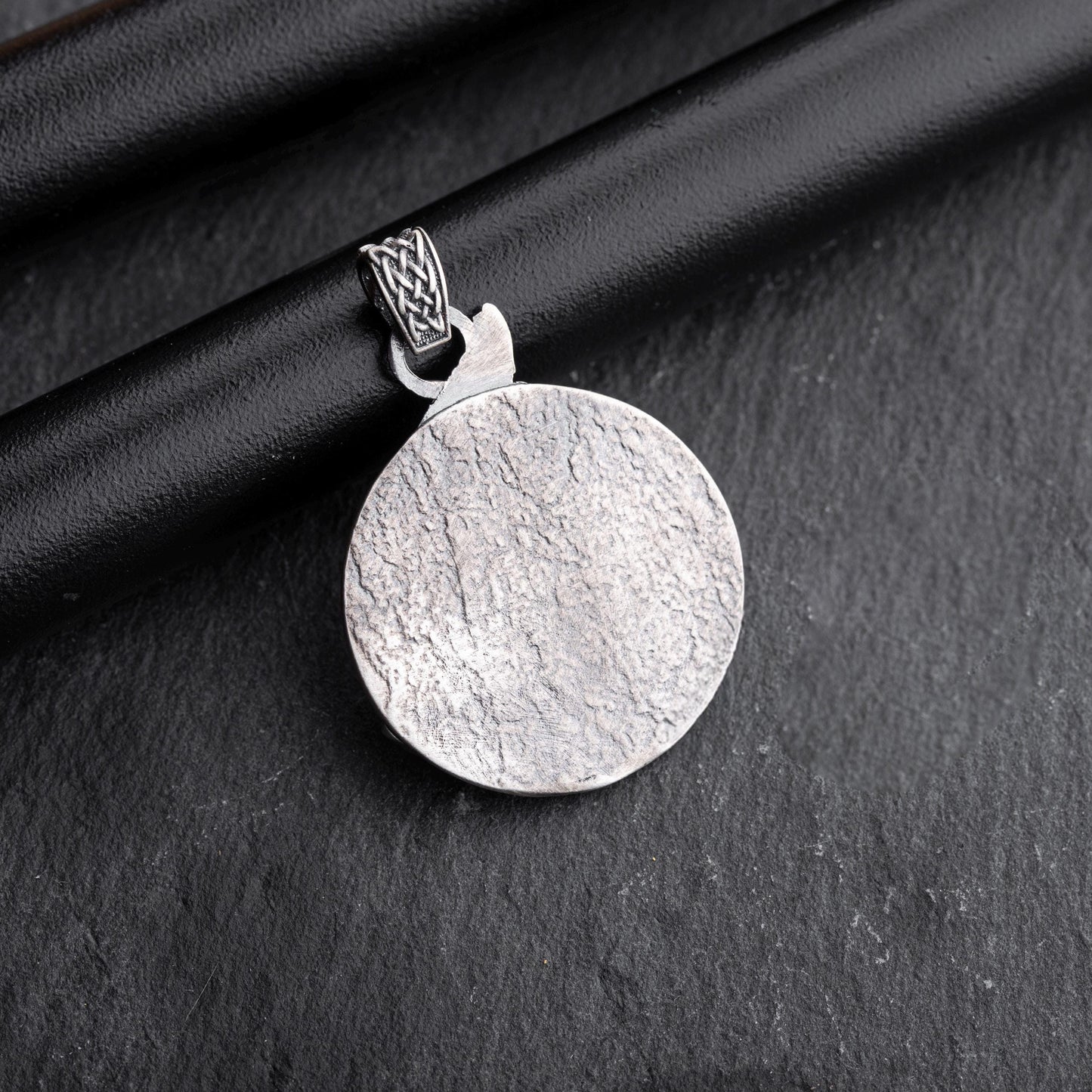 Gladiator Pendant featuring a round textured silver surface with an intricately designed bail, displayed on a dark textured background.