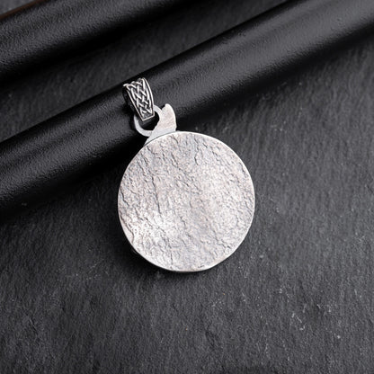 Gladiator Pendant featuring a round textured silver surface with an intricately designed bail, displayed on a dark textured background.