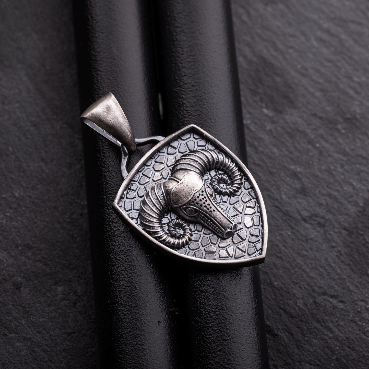 Close-up of an Aries Ram Pendant in silver, featuring a detailed ram's head with curled horns on a textured shield-shaped background with a loop for a chain necklace.