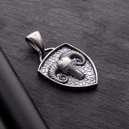 Aries Ram Pendant featuring a detailed ram's head with curled horns set on a textured silver shield-shaped background, showcasing intricate craftsmanship on a dark surface.