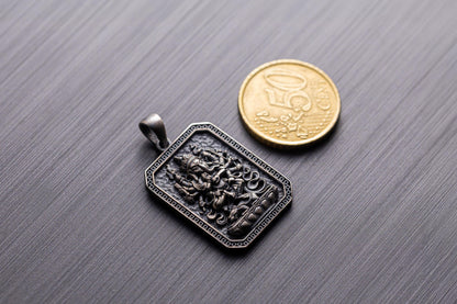 925 Silver Ganesha Pendant featuring detailed engraving of the Hindu deity Ganesha in a rectangular frame, shown beside a coin for size reference on a textured surface