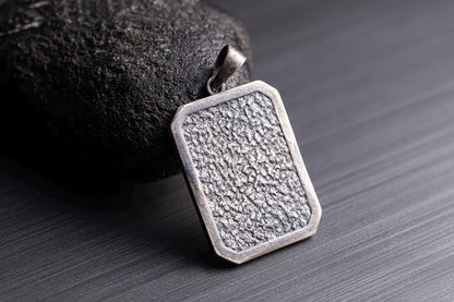 925 Silver Ganesha Pendant with a textured rectangular design, crafted from silver, resting against a dark stone background on a sleek surface.