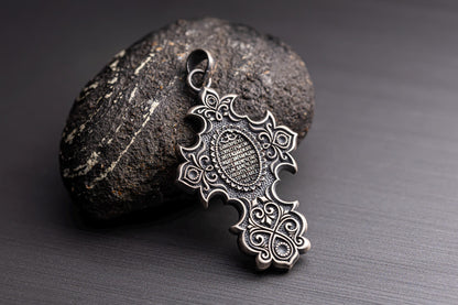Intricately designed Jesus Crucifix Pendant in silver tone resting against a textured dark stone, featuring detailed patterns and delicate scrollwork for a stylish look.