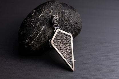 Sterling Silver Dragon Arrowhead Pendant resting on a textured black stone, featuring a detailed, rugged design with a silver frame and intricate chain necklace loop.